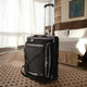 Black suitcase with wheels on a hotel room floor with bed and window in the background